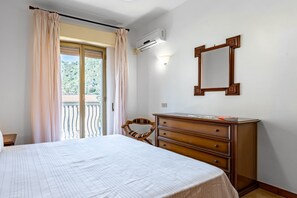 Une chambre à coucher comprenant un lit, une commode, une chaise, une fenêtre avec des rideaux et un appareil de climatisation.