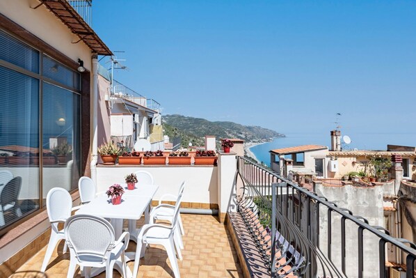 A balcony with a table and chairs, potted plants, and a view of the sea.