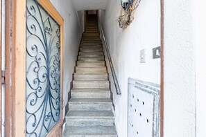 Eine Treppe führt zu einer oberen Etage, links eine Metallschranke und rechts ein an der Wand befestigtes Stromdosenfeld.