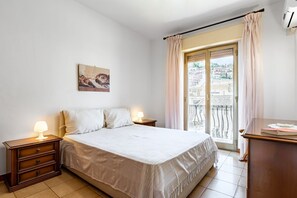 A bedroom with a bed, bedside tables, a window with curtains, and a balcony view.