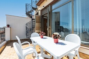 A balcony with a white table and chairs, potted plants, and a metal railing.