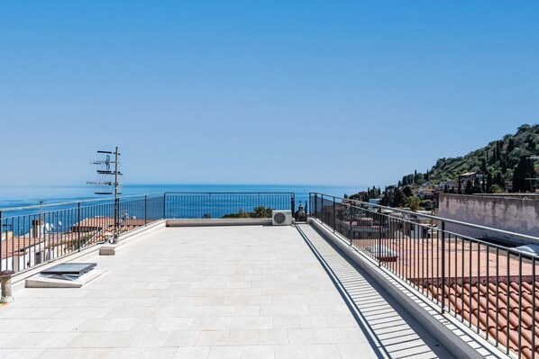 Eine Dachterrasse mit freiem Blick auf das Meer, einem Metallgeländer und einem gefliesten Boden.