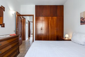 A bedroom with a large wooden wardrobe, a bed with white bedding, a dresser, and a nightstand with a lamp. - GuestHost - Spacious 81 sqm apartment in Taormina, ideal for 6 guests. Featuring two terraces from which to enjoy breathtaking sea views, this accommodation offers a unique experience. Perfectly situated just a short walk from the vibrant center of Taorm (Taormina)