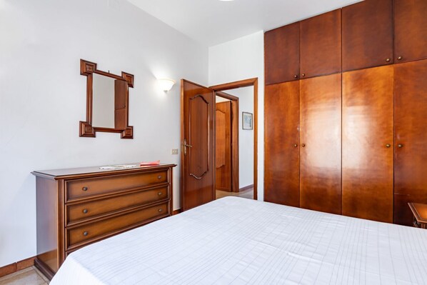 Une chambre à coucher comprenant un lit, une commode, un miroir, une armoire et une porte donnant sur une autre pièce.