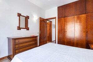 Ein Schlafzimmer mit Bett, Kommode, Spiegel, Kleiderschrank und einer Tür zu einem anderen Raum.