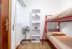 A bunk bed with a red frame, a white shelving unit, a standing fan, and a wooden door.