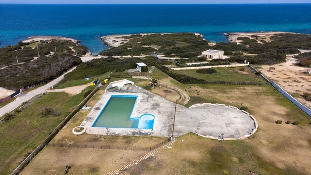 Vue aérienne d’une propriété dotée d’une piscine, d’un court de tennis et d’un grand espace extérieur offrant une vue sur l’océan.