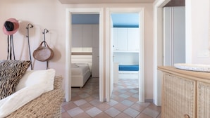 Une pièce comprenant un lit, un canapé en osier, une armoire en osier et une porte donnant accès à une salle de bain.