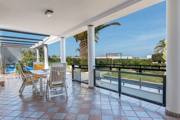 A covered outdoor area with a table and chairs, a railing, and a view of the landscape.