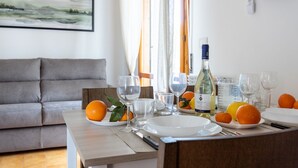 Een eettafel gedekt met borden, glazen en een fles wijn, met een grijze bank en een schilderij op de achtergrond.