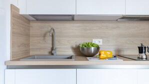 Een keuken met een roestvrijstalen spoelbak, een houten spatwand, een kom met groen, een gele paprika en een koffiezetapparaat.