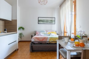 A compact room with a bed, a dining table with chairs, a kitchen area, and a window with curtains.