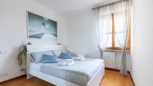 Een slaapkamer met een bed, een schilderij, een raam met gordijnen en een radiator.