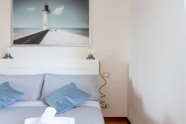 A bed with blue pillows, a white headboard, and a painting of a lighthouse above it.