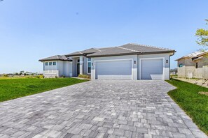 A modern two-story house with a paved driveway, garage doors, and a well-maintained lawn. - Gulf Access, Heated Saltwater Pool, Kayaks - Villa Sunset Lagoon (Cape Coral)