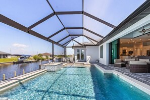 A swimming pool with a glass ceiling, a patio area with outdoor furniture, and a view of a residential neighborhood. - Gulf Access, Heated Saltwater Pool, Kayaks - Villa Sunset Lagoon (Cape Coral)
