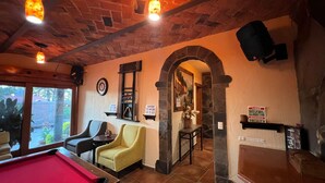 Una habitación acogedora con mesa de billar, asientos cómodos, chimenea de piedra y un reloj en la pared.