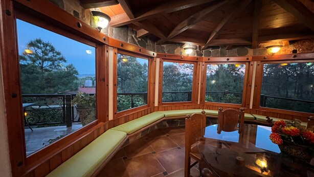 Un interior de cabaña acogedor con chimenea de piedra, bancos de madera y una mesa de comedor de vidrio.