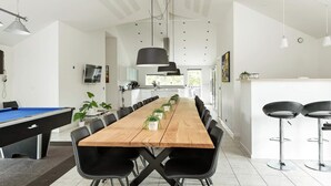 A modern dining area with a long wooden table, black chairs, and pendant lighting. - Beautiful home in Jerup with sauna (Jerup)