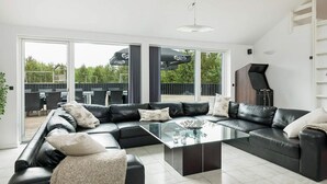 A modern living room with a sectional sofa, a glass coffee table, and a piano in the corner. - Beautiful home in Jerup with sauna (Jerup)