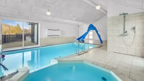 An indoor swimming pool with a blue slide, a shower area, and a view of the outdoors. - Beautiful home in Jerup with sauna (Jerup)