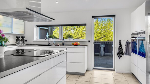 A modern kitchen with a large island, a built-in oven, and a window overlooking a balcony. - Beautiful home in Jerup with sauna (Jerup)