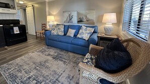 Een woonkamer met een blauwe bank, twee lampen, een rieten stoel en een vloerkleed.