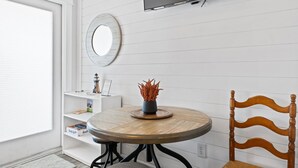 Een kamer met een ronde houten tafel, een houten stoel, een aan de muur bevestigde televisie en een plank met boeken en een decoratief object.
