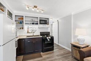 A compact kitchen with a built-in microwave, stove, and shelves above the counter. - 1bd 1ba Family Friendly Pool Walk to Restaurants (Panama City Beach)