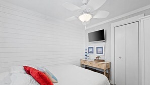 Een slaapkamer met een bed, een plafondventilator, een aan de muur bevestigde televisie, een houten dressoir en een garderobe.
