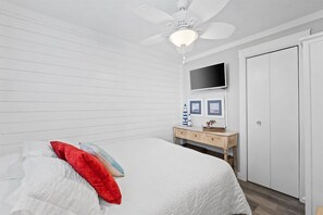 Une chambre à coucher comprenant un lit, un ventilateur de plafond, un téléviseur fixé au mur, une commode et une armoire.