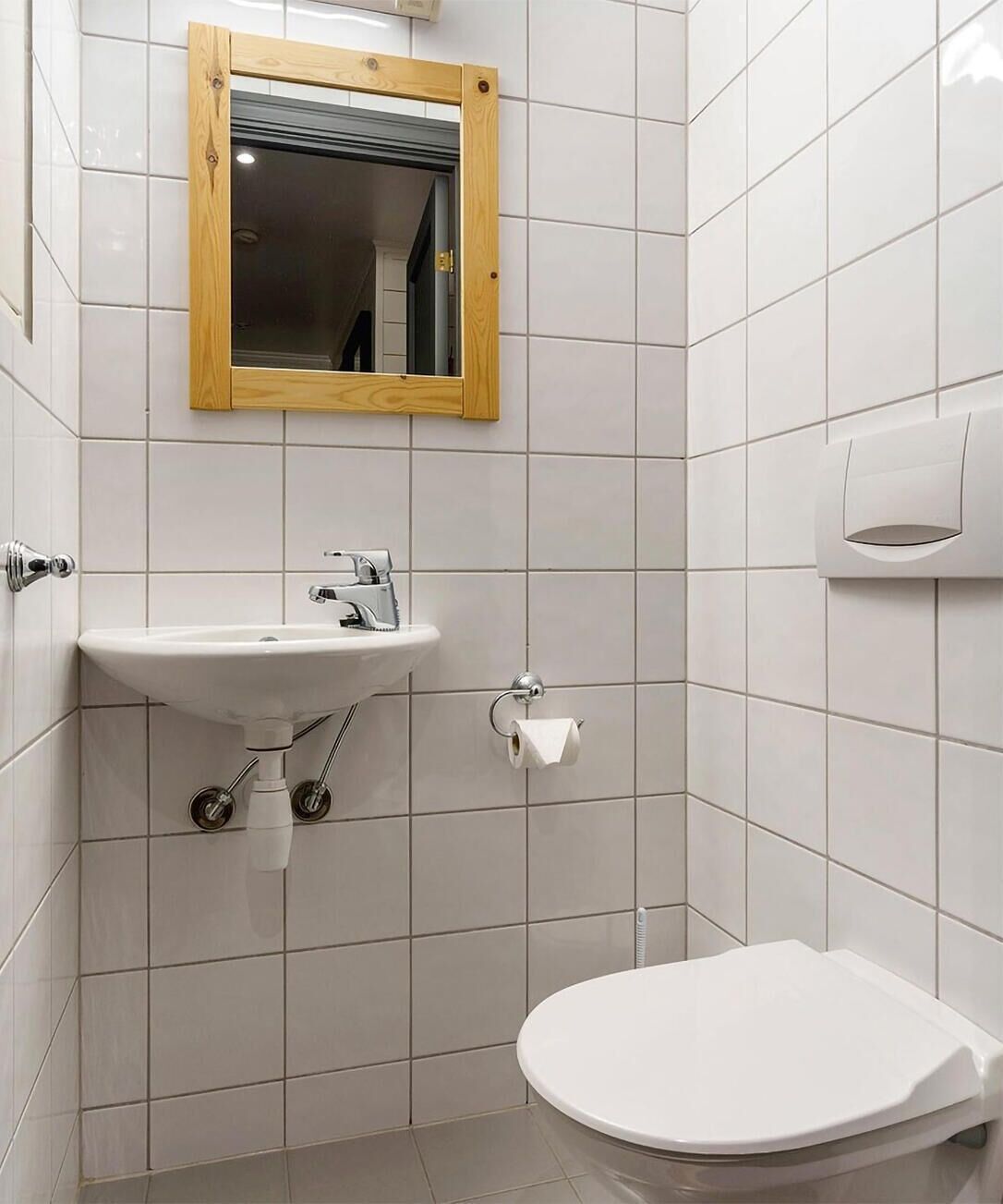 A small, clean bathroom with a white sink, toilet, and a wooden-framed mirror.