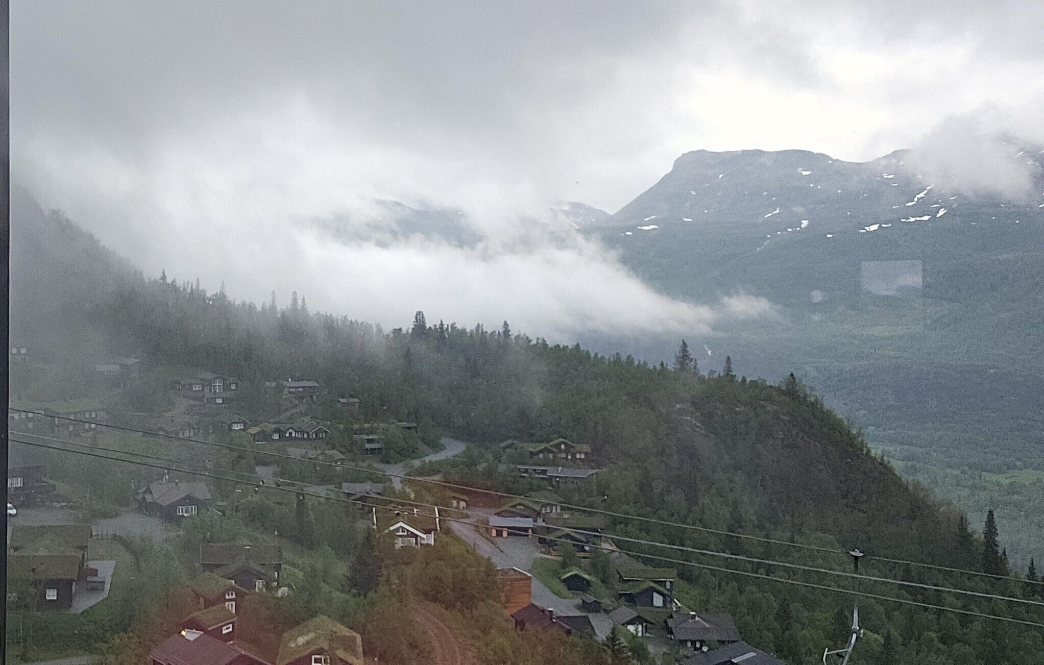 Un village de montagne où les maisons sont nichées au milieu des arbres, avec une route sinueuse et une ligne de téléphérique.