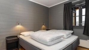Ein Schlafzimmer mit einem Bett, zwei Nachttischen, einem Fenster mit Vorhängen und einer Wandlampe.