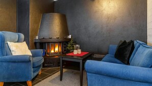 Ein modernes Wohnzimmer mit Kamin, zwei blauen Sesseln, einem kleinen Tisch und einer dunkel gestrichenen Wand.