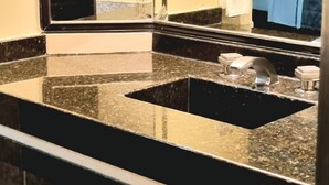 Une salle de bain avec un grand miroir, un comptoir en granit, un lavabo et un porte-serviettes.