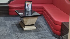 Un canapé rouge, une table noire devant, un tableau encadré au mur et un sol recouvert d’une moquette.