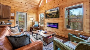 A cozy cabin interior with a wooden ceiling, a fireplace, a dining area, and a view of the outdoors.