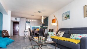 Ein modernes Wohnzimmer mit Sofa, Couchtisch und Sesseln. Im Hintergrund befindet sich eine Küche mit Essbereich.