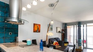 Eine moderne Küche mit einer zentralen Kochinsel, ein Essbereich mit einem dunklen Sofa und ein Wohnzimmer mit einem großen Fenster.