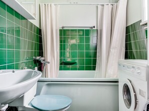 A bathroom with green tiles, a white sink, a blue toilet, and a washing machine.