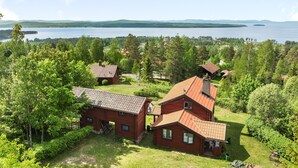 A red wooden cabin with a sloped roof, surrounded by lush greenery and a lake view. - Vacation home Alice by Interhome (Tällberg)