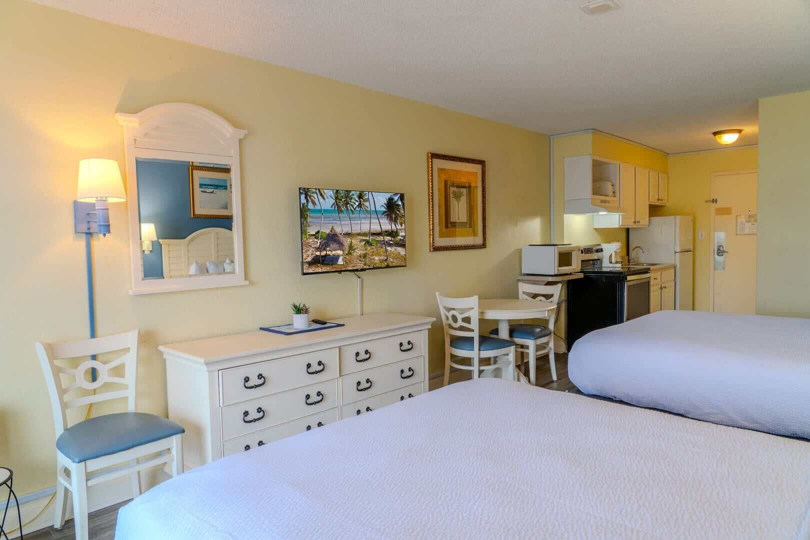 A hotel room with two beds, a desk, a chair, a small table, a microwave, and a refrigerator.