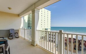 A balcony with a view of the beach and a tall building in the background.