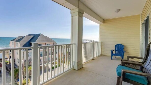 A balcony with a view of the ocean, a chair, and a table.