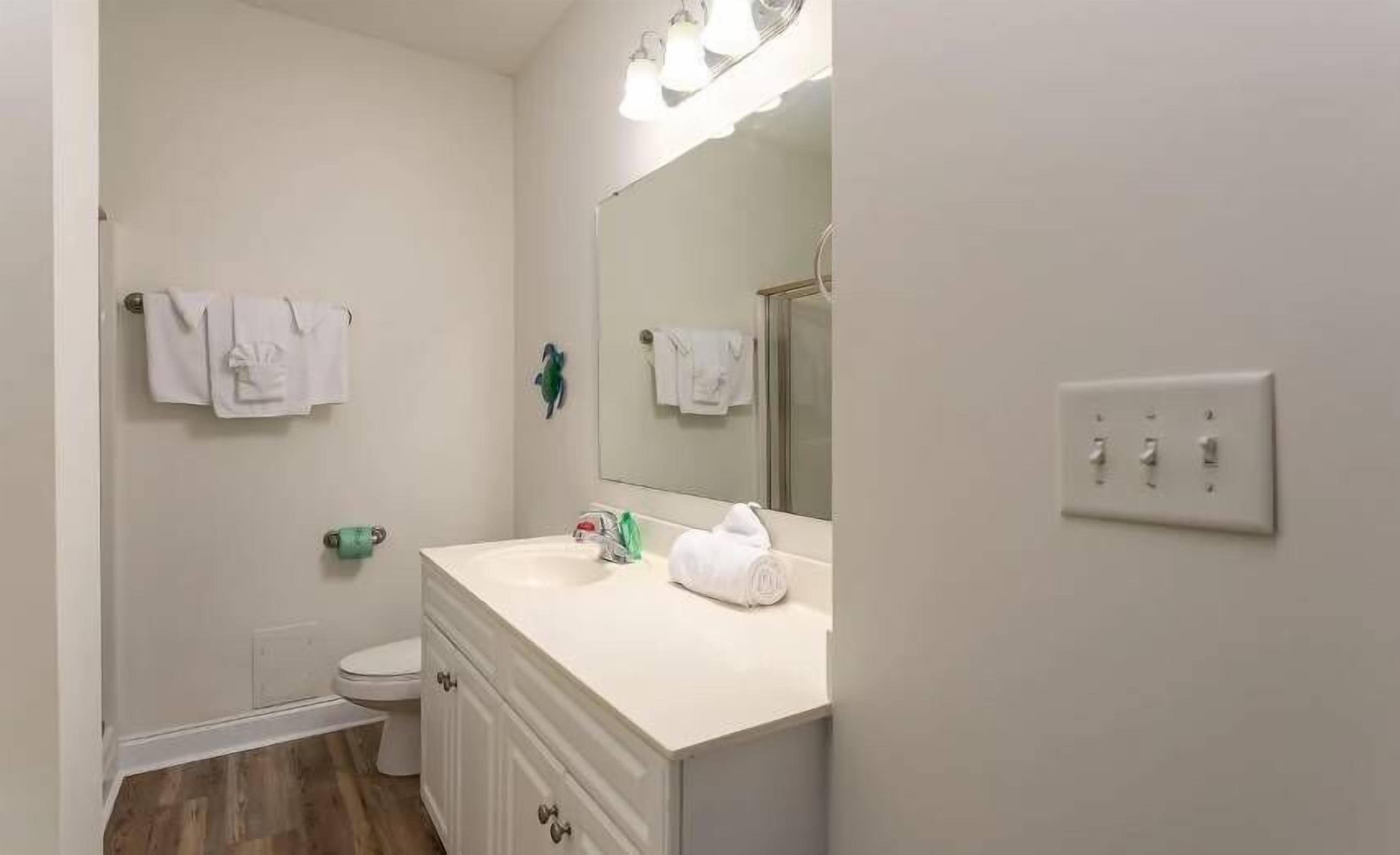 A bathroom with a toilet, sink, mirror, and towel rack.