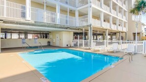 A multi-story hotel with a swimming pool, balconies, and a beachside view.