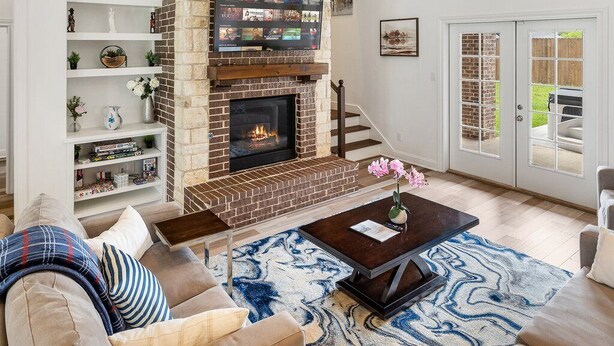 A modern living room with a brick fireplace, a large window, and a staircase leading to an upper level.