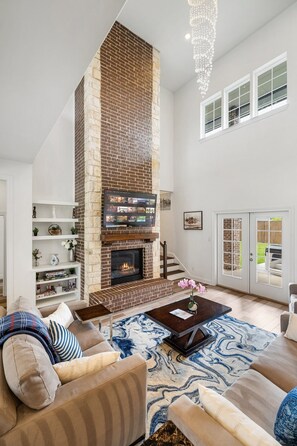 A modern living room with a brick fireplace, a large window, and a staircase leading to an upper level. - Lakeview Oasis Home with Spa near Lake Lewisville  (Lakewood Village)