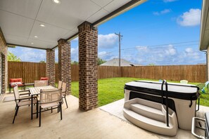 Un patio techado con un pilar de ladrillo, mobiliario exterior y un jacuzzi.